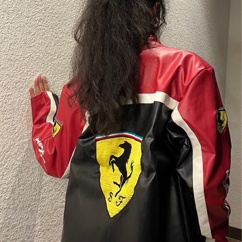 Person wearing a red and black Ferrari jacket against a plain wall.